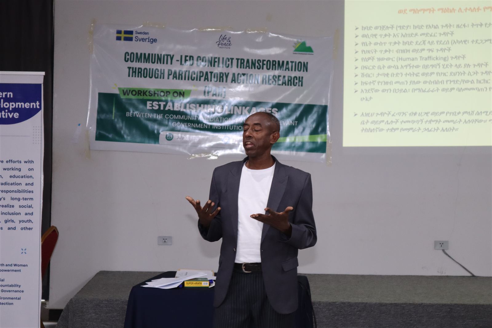 Speaker presenting beside a slide listing categories of community disputes in Amharic
