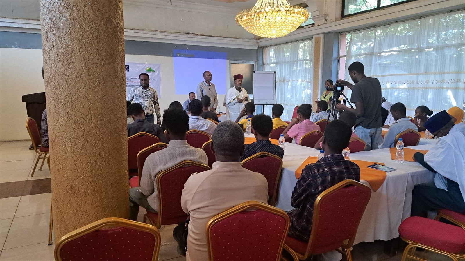 Facilitator beside a hand-written Amharic flipchart agenda and a sticky-note exercise