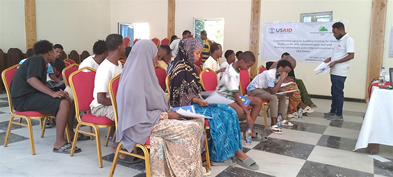 Group of youth seated in a hotel meeting room with a USAID and EDI banner naming the life-skills training