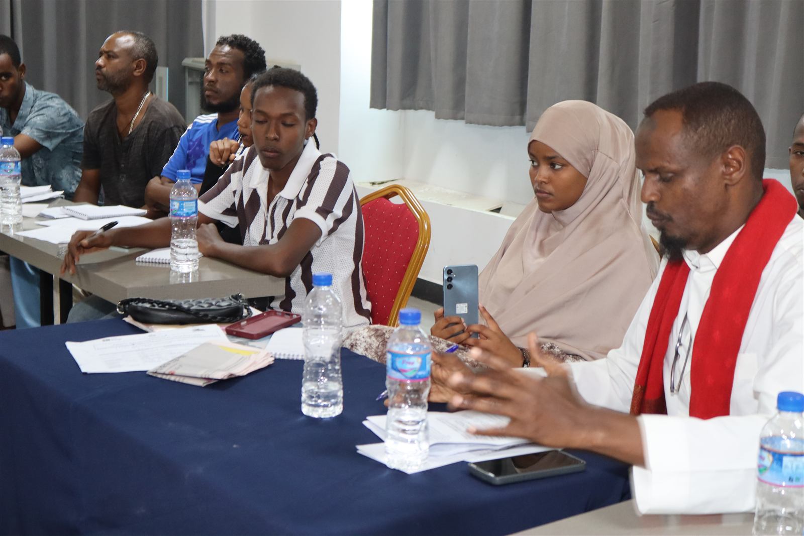 Mixed-age group seated around tables with notebooks, one participant wearing a red scarf