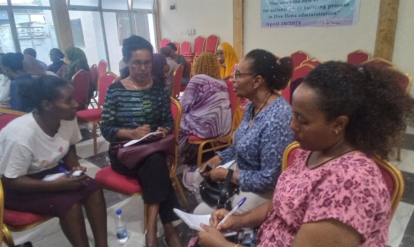 Four women and one man in animated discussion on red chairs, banner visible behind them