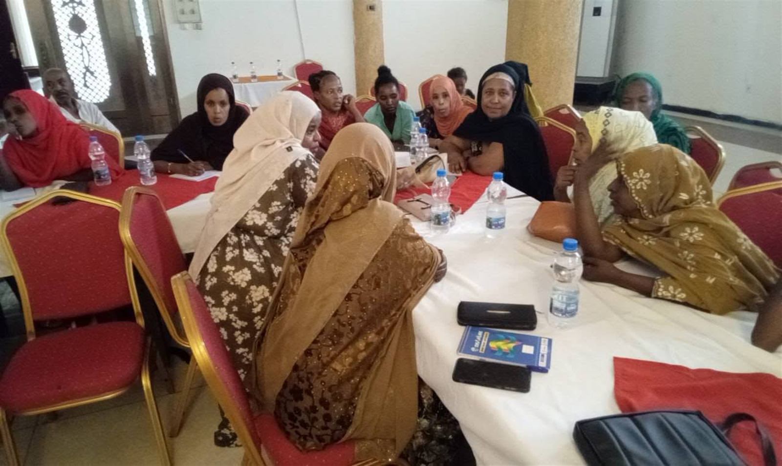 Circle of women in colorful headscarves in animated small-group discussion at a round table