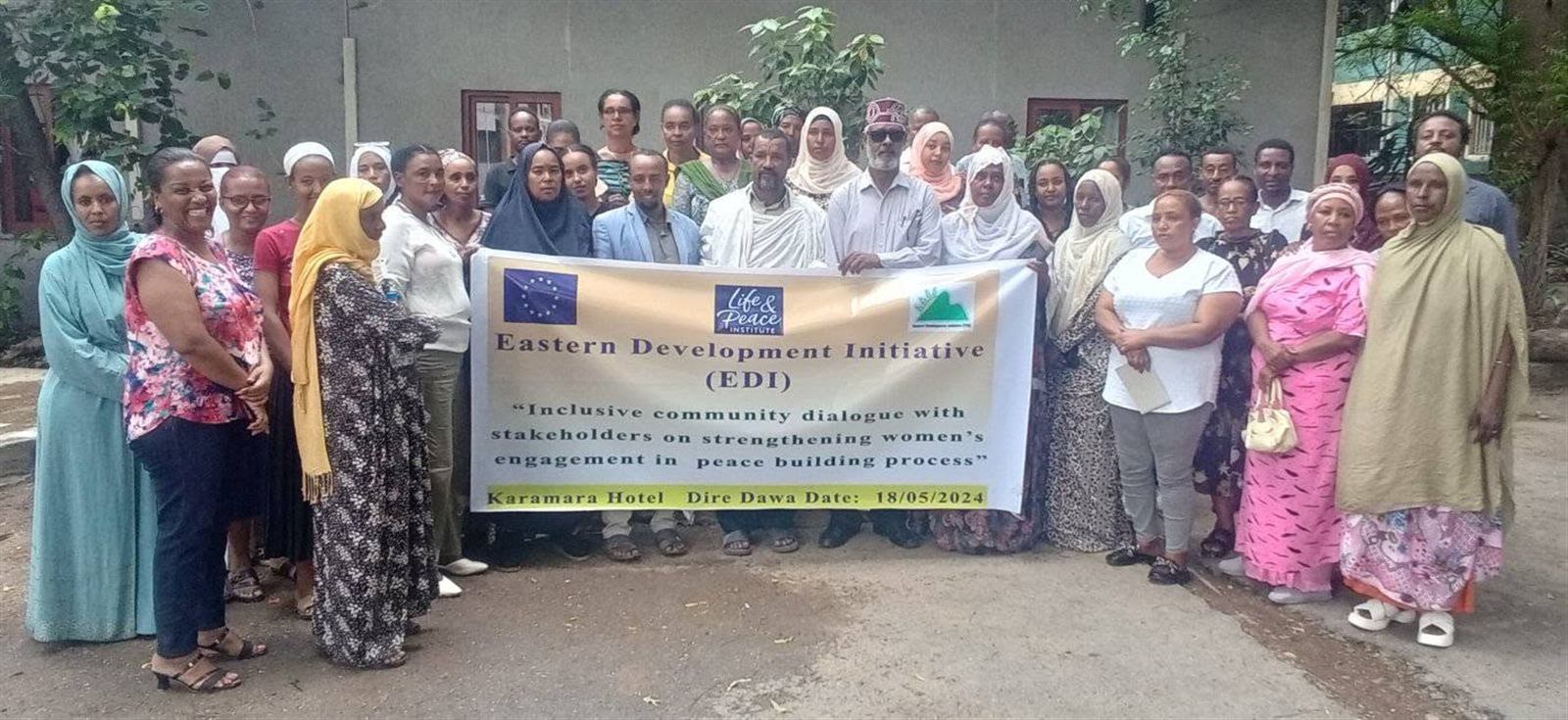 Large mixed group posed outdoors holding the Inclusive Community Dialogue banner, May 18 2024