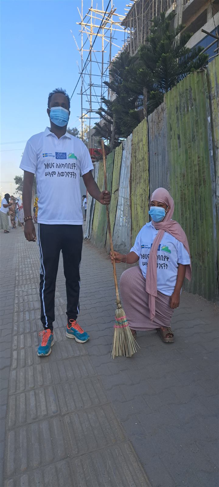 Two women in matching white T-shirts and masks standing on a palm-lined street