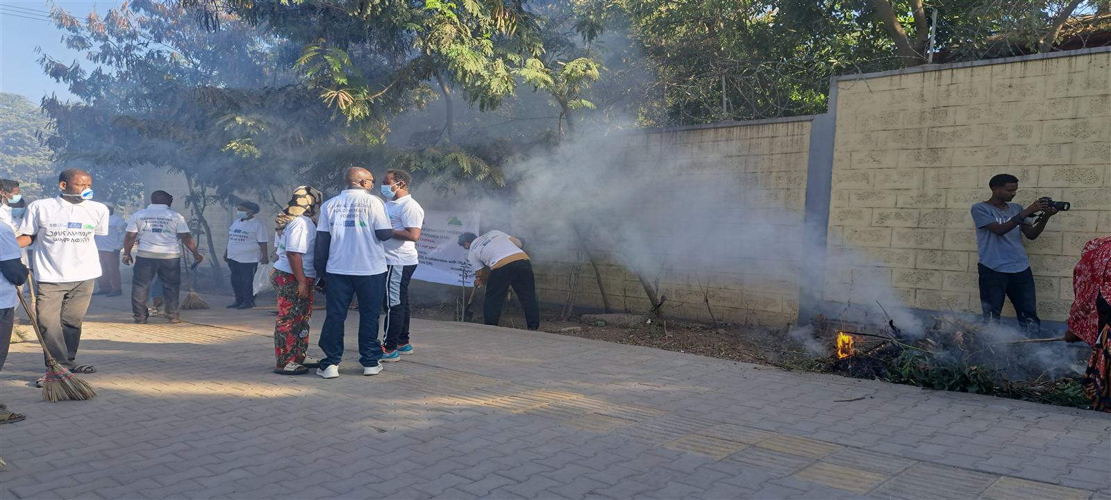 Group of about eight participants in Cleaning Together, Building Peace Forever T-shirts walking together carrying brooms