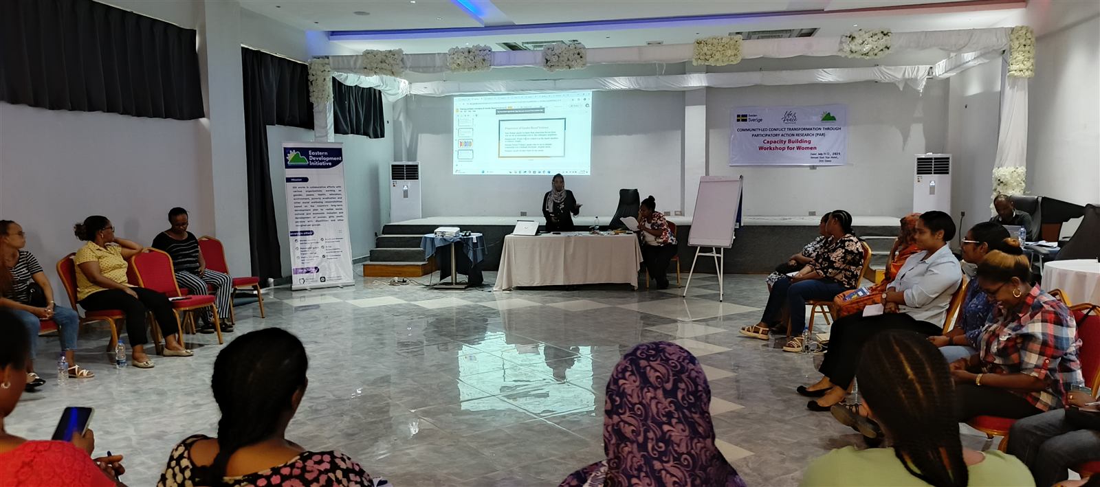 Two facilitators beside a projected slide titled Perpetrators of Gender Based Violence