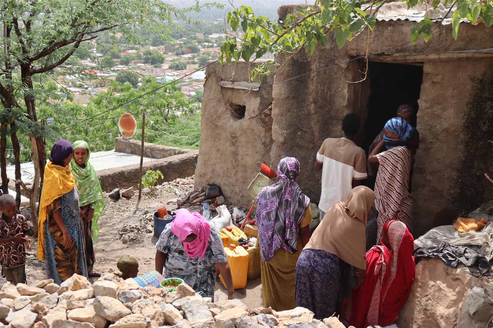 Several women arriving at a stone house carrying yellow water jerry cans